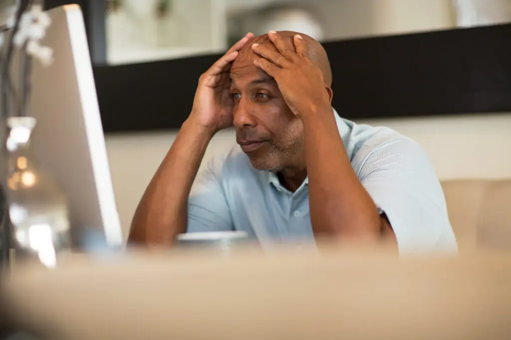 African American man working from his home office frustrated with his hands up on the side of his head