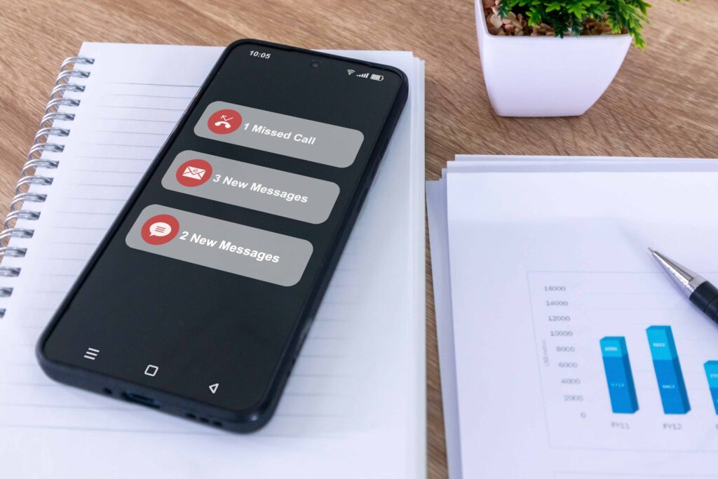 picture of wooden desk with white notepad and black phone showing 1 missed calls, and 5 new messages