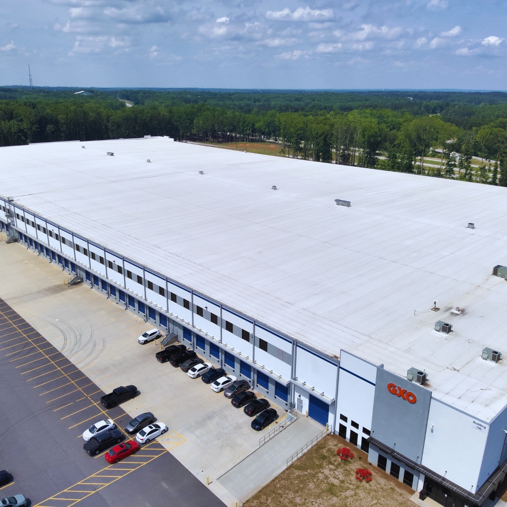 Aerial shot taken of white and gray GXO warehouse in Flowery Branch, GA with a few cars in the parking lot.
