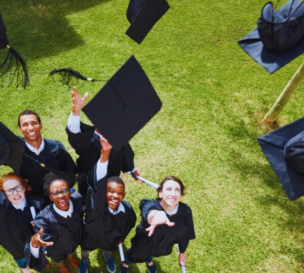Stock image of a group of graduates in black gowns throwing up black graduation caps and smiling
