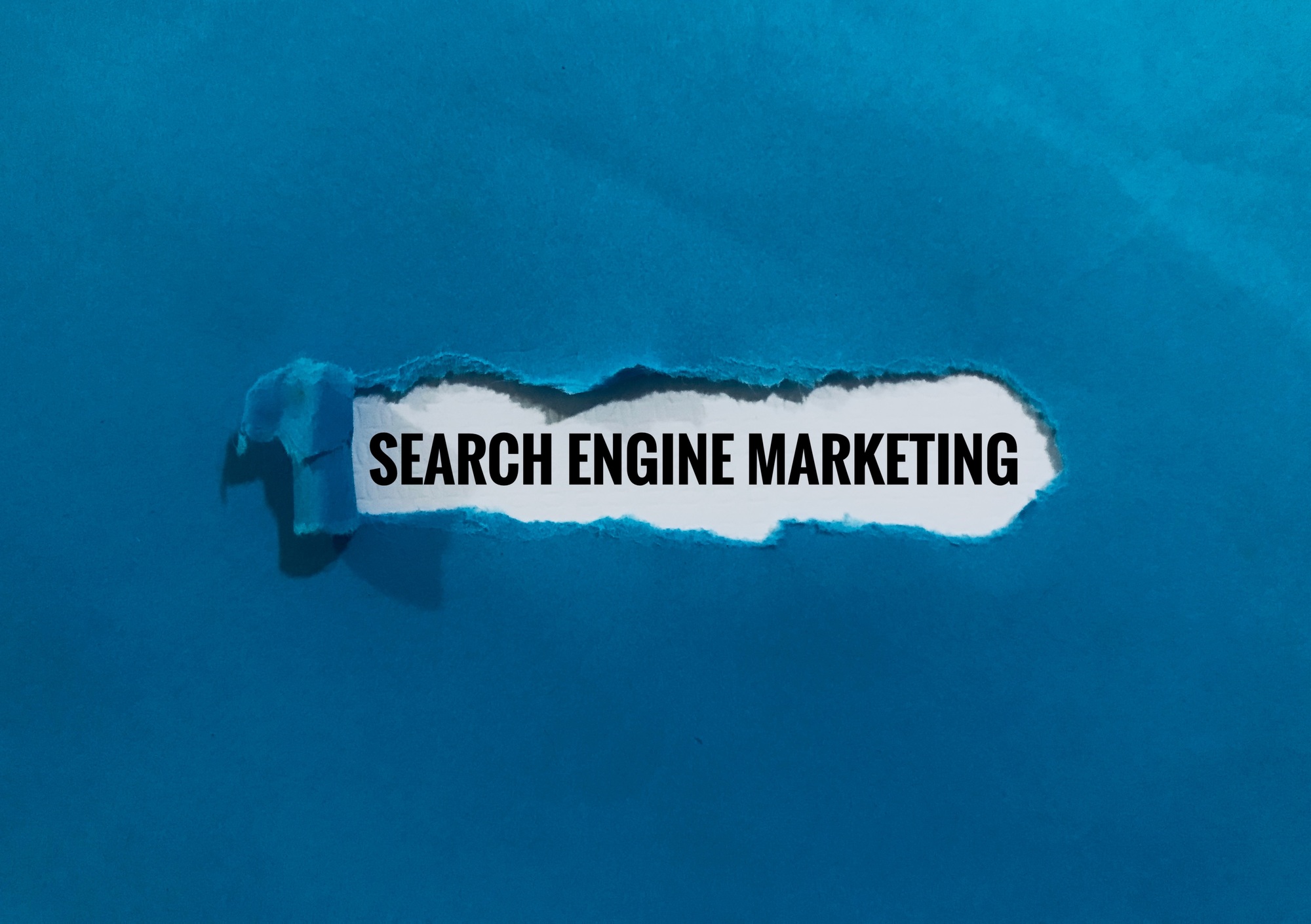 sky blue paper ripped in the middle to show the words Search Engine Marketing