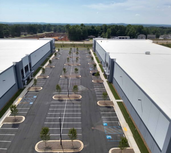 Aerial view of 2 white and gray warehouses divided by freshly done parking lot
